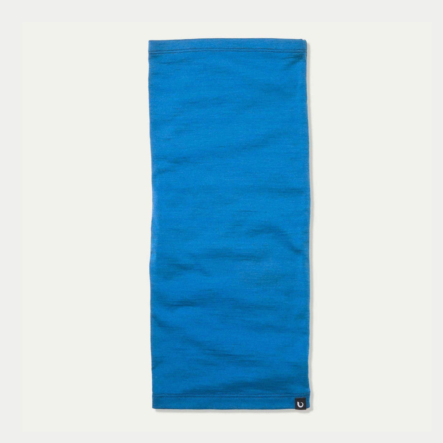 Arctic blue Merino neck gaiter laid flat against a light off-white background, featuring a small Bluey Merino horn logo patch on the bottom right corner.