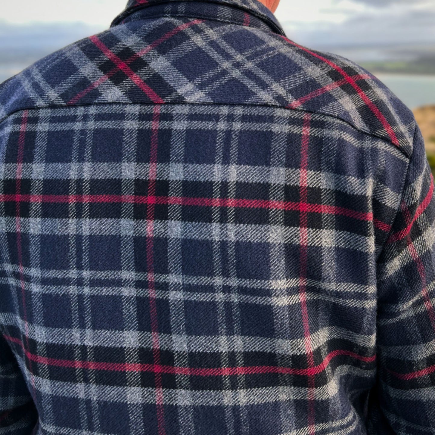 Person wearing the Stanley Overshirt in Navy, red and grey plaid shirt with a scenic background © Bluey Merino Tasmania