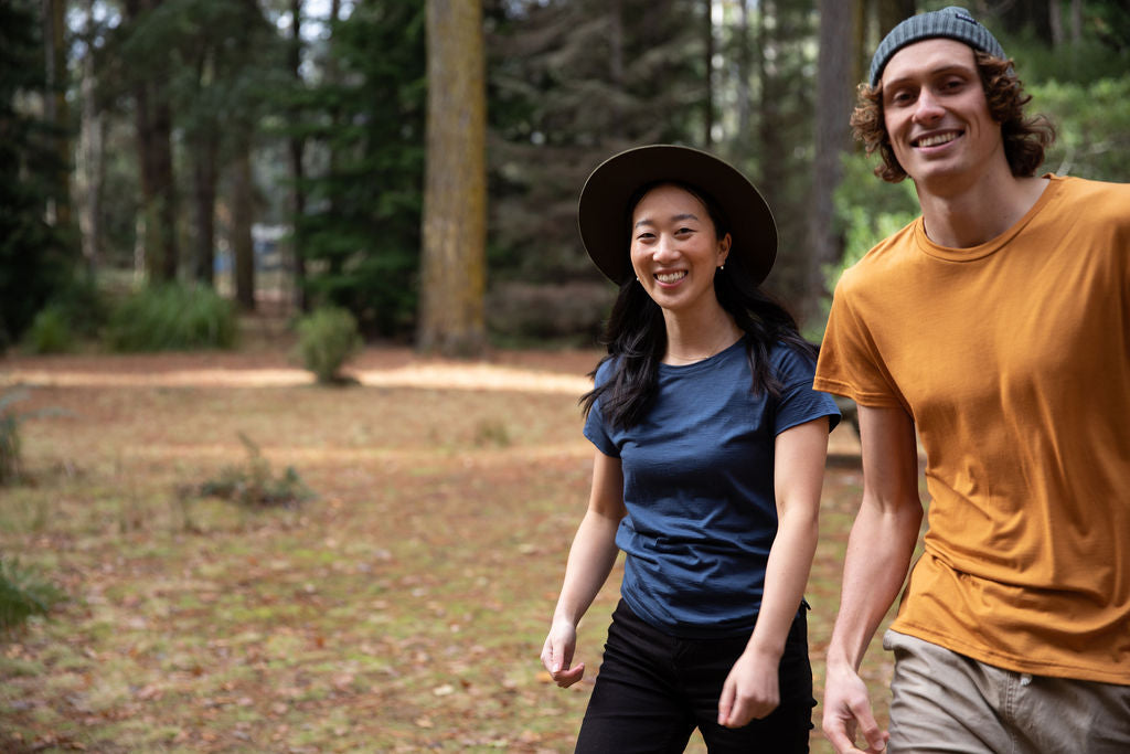 Two persons are happy walking in a beautiful forest. They are both wearing Bluey Merino t-shirts. 
