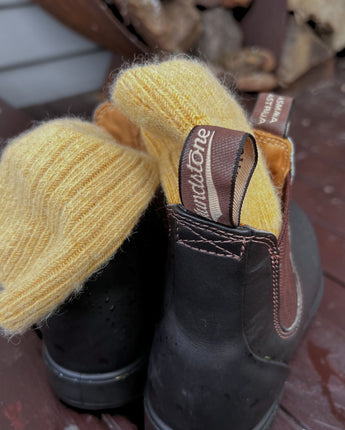 Soft Alpaca wool yellow socks sitting in a pair of Blundstone boots by the wood fire stand on a cabin in Tasmania © Bluey Merino Tasmania