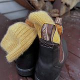 Soft Alpaca wool yellow socks sitting in a pair of Blundstone boots by the wood fire stand on a cabin in Tasmania © Bluey Merino Tasmania