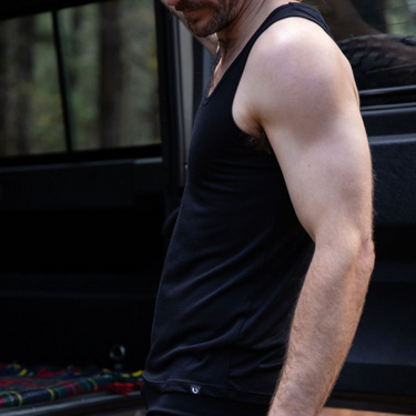 Steve is wearing the Men's Tasmanian Merino 150 Tank Top  in Currawong (black). He is standing next to the Land Rover 110 - Photography by Melanie Kate Creative -  © Bluey Merino
