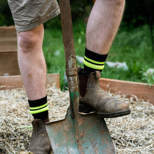 Person wearing brown boots and Wool Blend black socks with yellow fluro stripes, standing next to a shovel outdoors. © Humphrey Law
