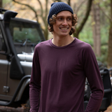 Hamish is wearing the Men’s Tasmanian Merino 180 Raglan Long Sleeve Top in Dark Bridestowe with the Fisherman Beanie in Navy. He is smiling, relaxed with hands in pockets standing in front of BLU the Defender 110 - Photography by Melanie Kate Creative -  © Bluey Merino