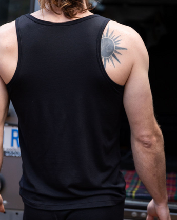 Steve is wearing the Men's Tasmanian Merino 150 Tank Top in Currawong (black). Classic singlet cut. Steve is showing his back to us and is standing in front of BLU the Land Rover 110 - Photography by Melanie Kate Creative - © Bluey Merino