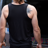 Steve is wearing the Men's Tasmanian Merino 150 Tank Top in Currawong (black). Classic singlet cut. Steve is showing his back to us and is standing in front of BLU the Land Rover 110 - Photography by Melanie Kate Creative - © Bluey Merino