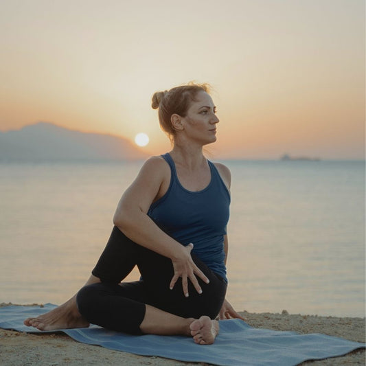 Woman practicing yoga on a beach at sunset wearing Bluey's Merino Core tank top in the colour Tasman (French Blue) © Bluey Merino Tasmania