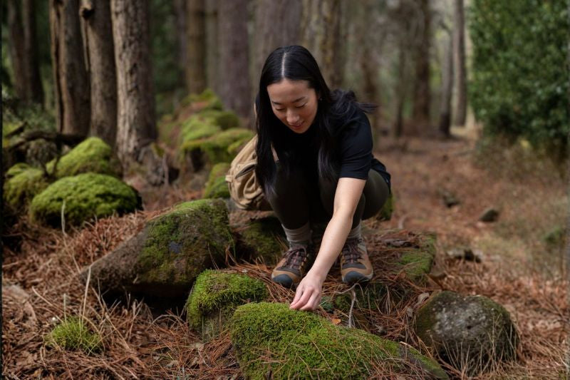 Person in a forest setting examining moss-covered stones - Tasmanian wilderness. © Bluey Merino Tasmania