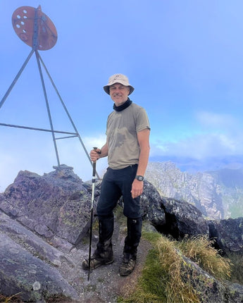 Man hiking on top of Mount Murchison with a scenic view in the background. He is wearing Bluey's Emrik t-shirt in the colour West Coast. Image © Simon + Lisa Ross for Bluey Merino Tasmania.