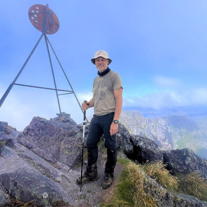 Man hiking on top of Mount Murchison with a scenic view in the background. He is wearing Bluey's Emrik t-shirt in the colour West Coast. Image © Simon + Lisa Ross for Bluey Merino Tasmania.