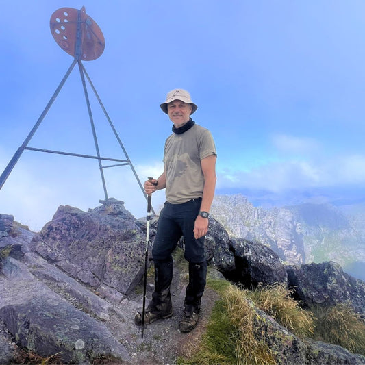Man hiking on top of Mount Murchison with a scenic view in the background. He is wearing Bluey's Emrik t-shirt in the colour West Coast. Image © Simon + Lisa Ross for Bluey Merino Tasmania.