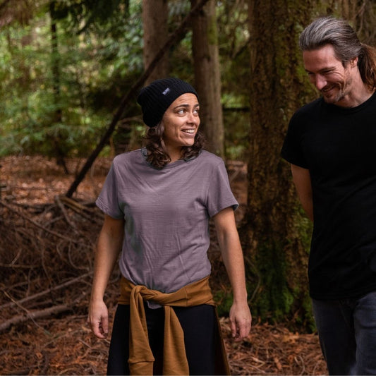 Two people standing in a forest, one wearing a Marron Merino t-shirt and black Bluey beanie, the other in a black Merino t-shirt. © Bluey Merino Tasmania