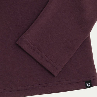Close-up of a maroon long-sleeve shirt with a brand logo on a white background