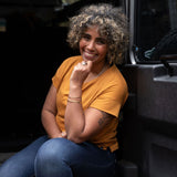 Smiling women sitting at the back of a defender 110 is wearing a limited edition of the Klara top in the colour billy button (mustard yellow) © Bluey Merino Tasmania