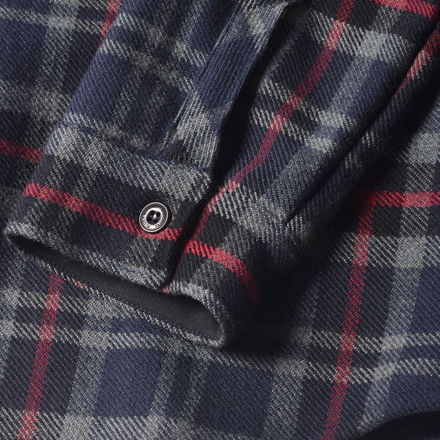 Close-up of a plaid fabric and © Bluey Merino Tasmania button. Plaid is red, grey and navy patterns