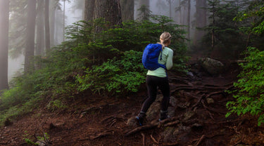 Person wearing a Merino base-layer with a blue backpack hiking through a misty forest.