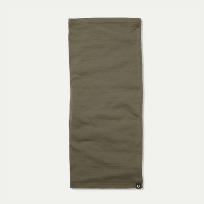 An light sage green Merino neck gaiter laid flat against a light off-white background, featuring a small black Bluey Merino logo patch on the bottom right hem. © Bluey Merino Tasmania