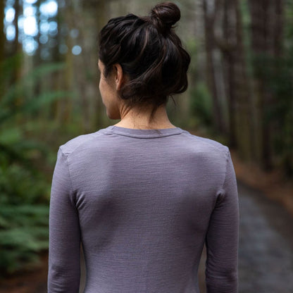 Woman standing in northern Tasmania wilderness wearing the 160 Merino Hike in the colour dusk. She has a back turned and is looking at the forest  © Bluey Merino Tasmania