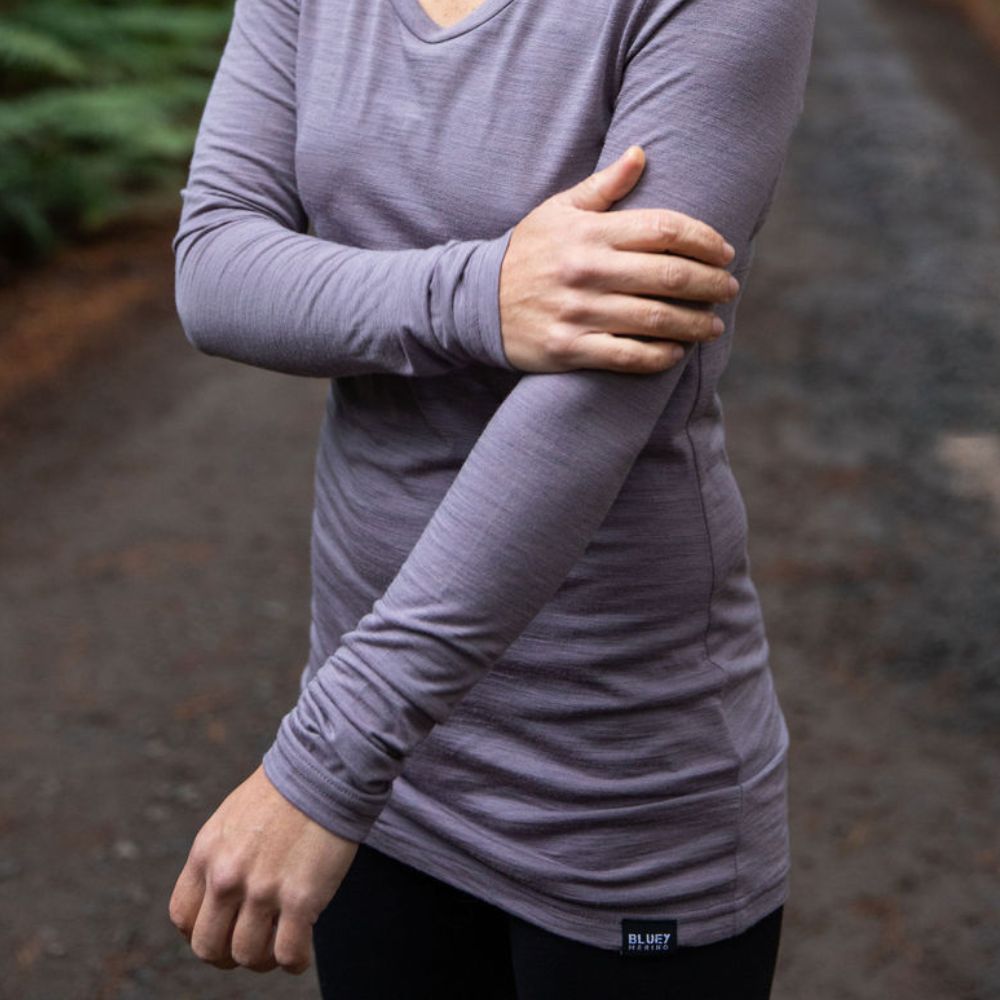 Up close woman standing in northern Tasmania wilderness wearing the 160 Merino Hike in the colour dusk. She is feeling the softness of the fabric with her hand © Bluey Merino Tasmania