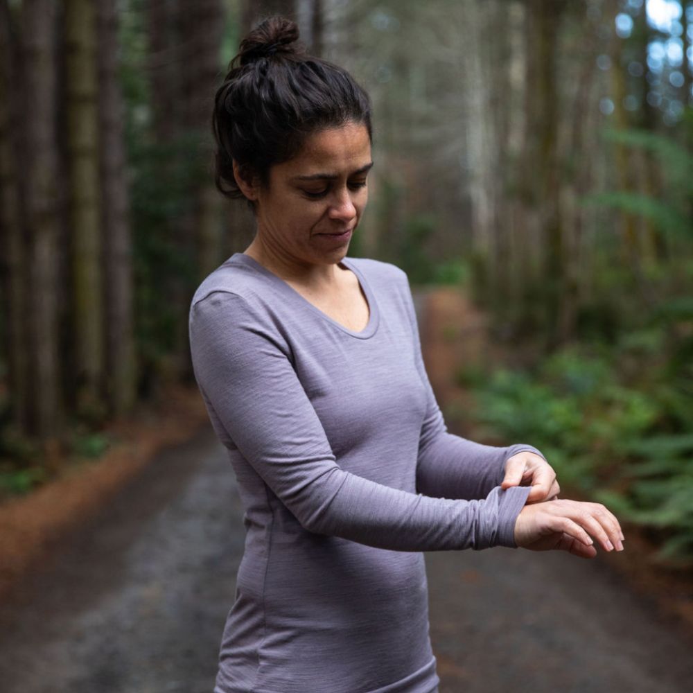 Woman standing in northern Tasmania wilderness wearing the 160 Merino Hike in the colour dusk. She is feeling the softness of the fabric with her hand © Bluey Merino Tasmania