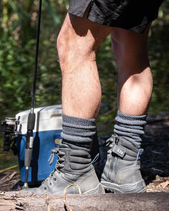 Person wearing hiking boots and socks standing on a log with a cooler and fishing rod in the background. XHF_Thermal Wool Sock. © Humphrey Law. Made in Australia.
