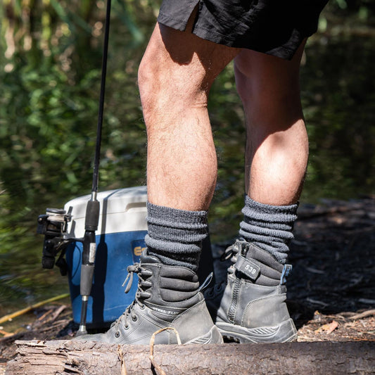Person wearing hiking boots and socks standing on a log with a cooler and fishing rod in the background. XHF_Thermal Wool Sock. © Humphrey Law. Made in Australia.